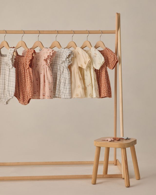 Wooden clothing rack with baby dresses on a beige background