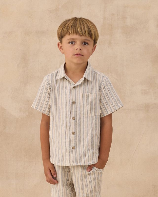 Young boy wearing a striped shirt and pants against a beige background