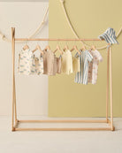 Children's clothing on a wooden rack against a light green wall.