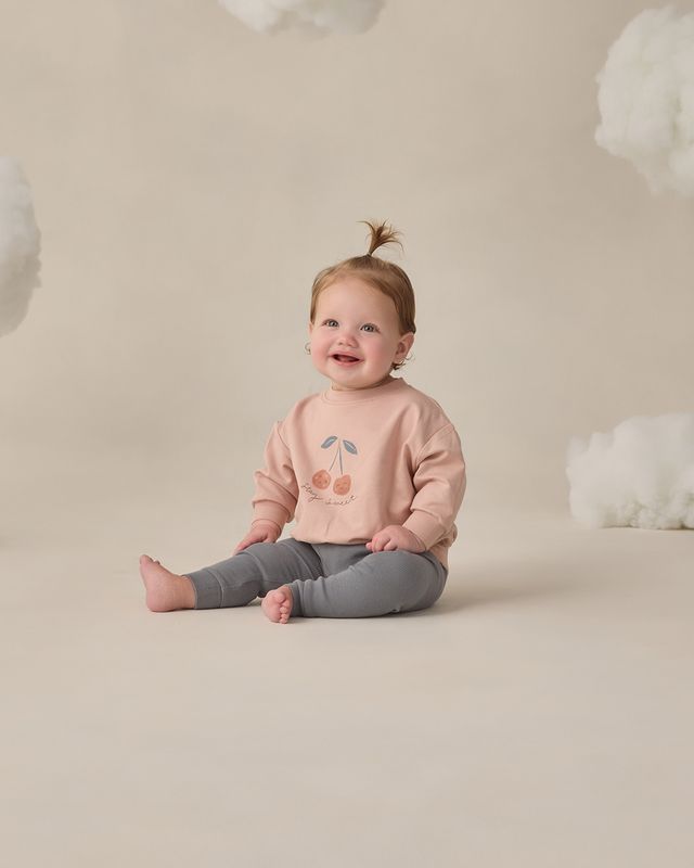 Child wearing a pink sweater with a cherry design on a beige background