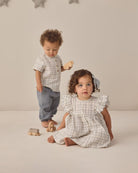 Two children in matching plaid outfits standing on a neutral background