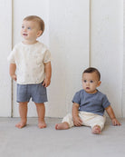 Two young children wearing casual clothing against a white wooden panel background