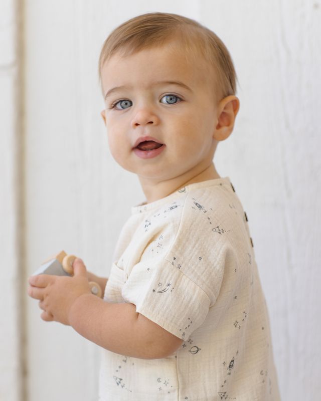 Baby wearing a light-colored outfit with a subtle pattern against a plain background