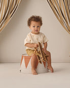 Child sitting on a small stool with a wooden toy airplane