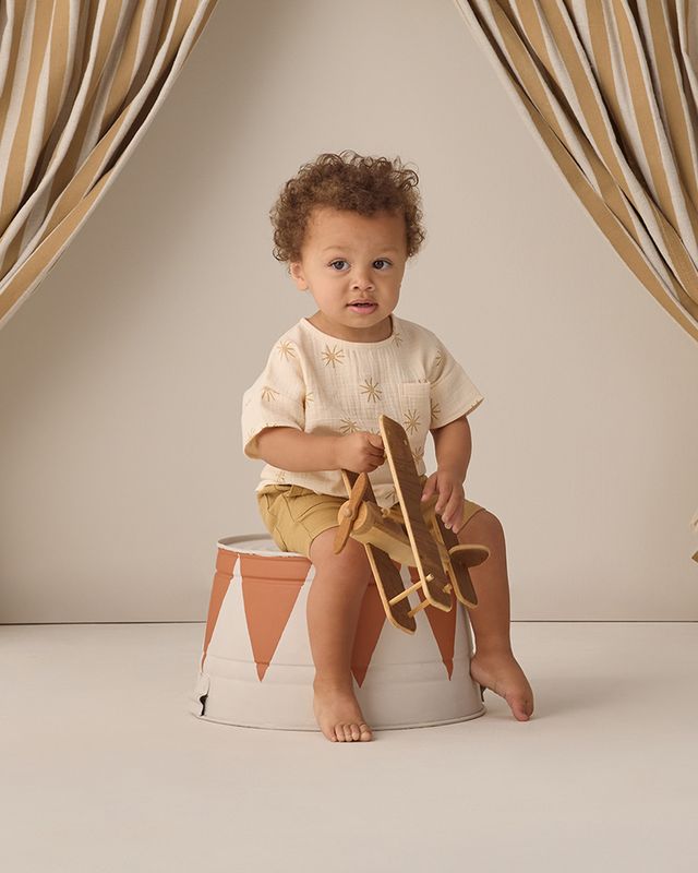 Child sitting on a small stool with a wooden toy airplane