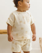 Baby wearing a cream-colored outfit with gold star patterns on a neutral background