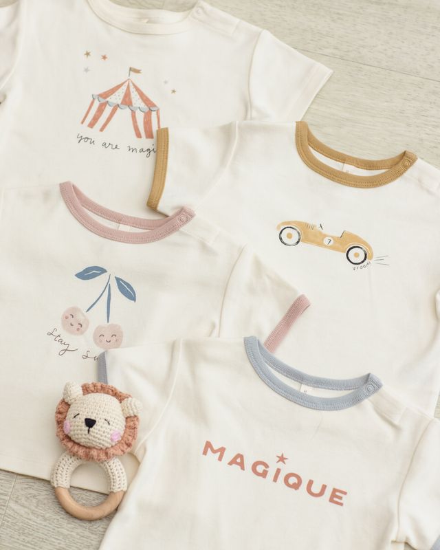 Two baby onesies with cartoon designs and a lion rattle on a textured surface.