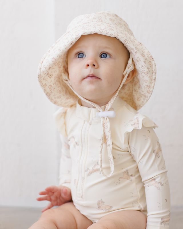 Baby wearing a cream-colored hooded outfit with a plain background