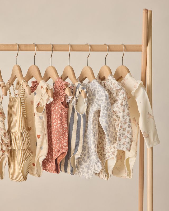 Collection of baby clothes on hangers against a beige wall