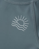 Close-up of a blue garment with a white sun and wave design on a matching background.