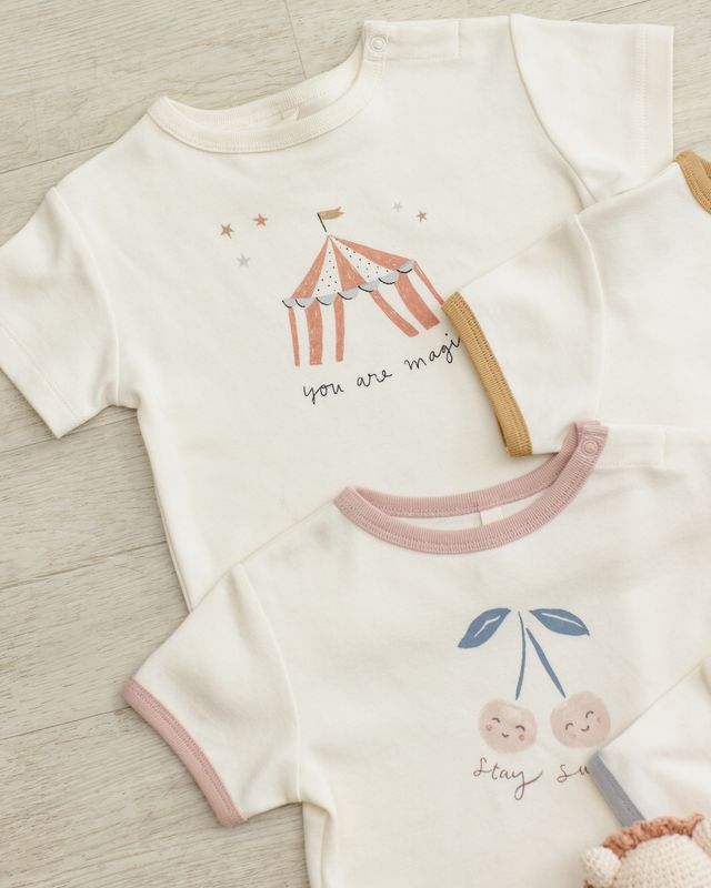 Two children's shirts with circus tent and cherry designs on a wooden surface