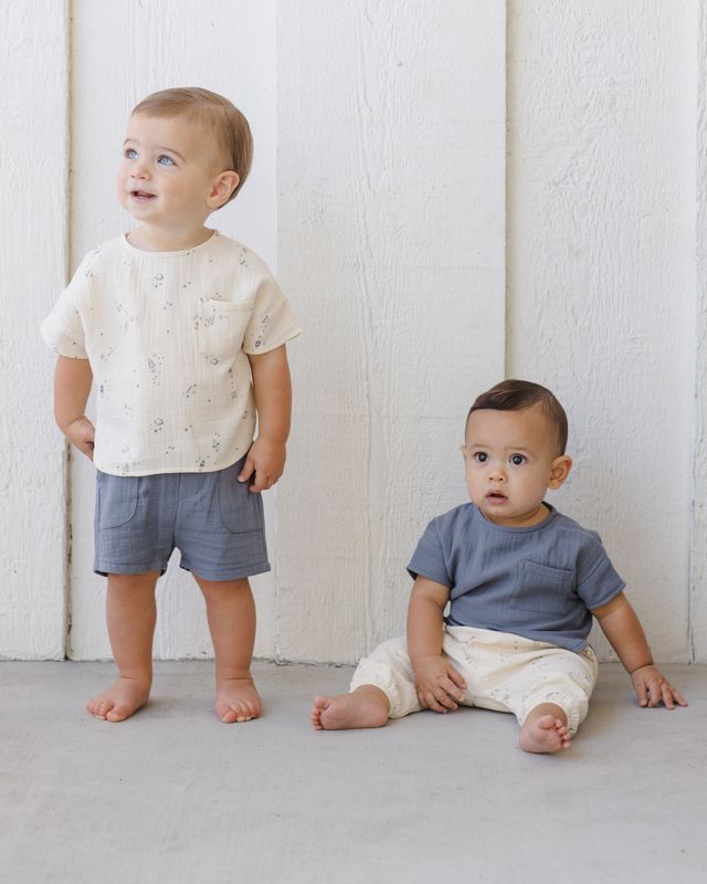 Two young children wearing casual clothing against a white wooden panel background