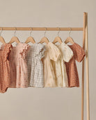 Row of children's dresses on hangers against a beige wall