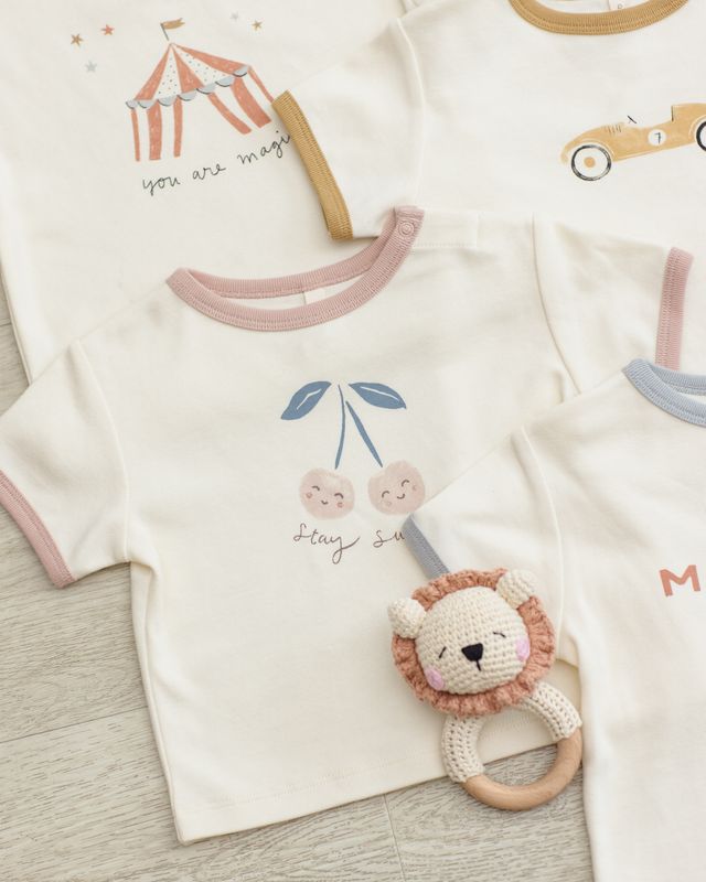 Baby outfit with lion rattle on a wooden surface