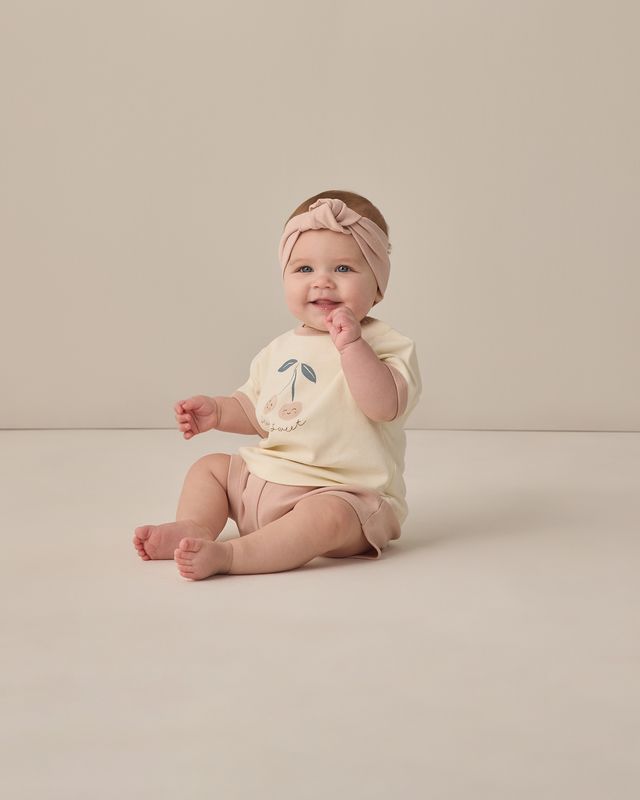 Baby sitting on a plain background wearing a light-colored outfit with a floral design.