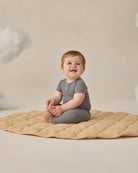 Baby sitting on a beige blanket against a neutral background
