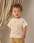 Child wearing a beige shirt with gold star patterns in front of a curtain.