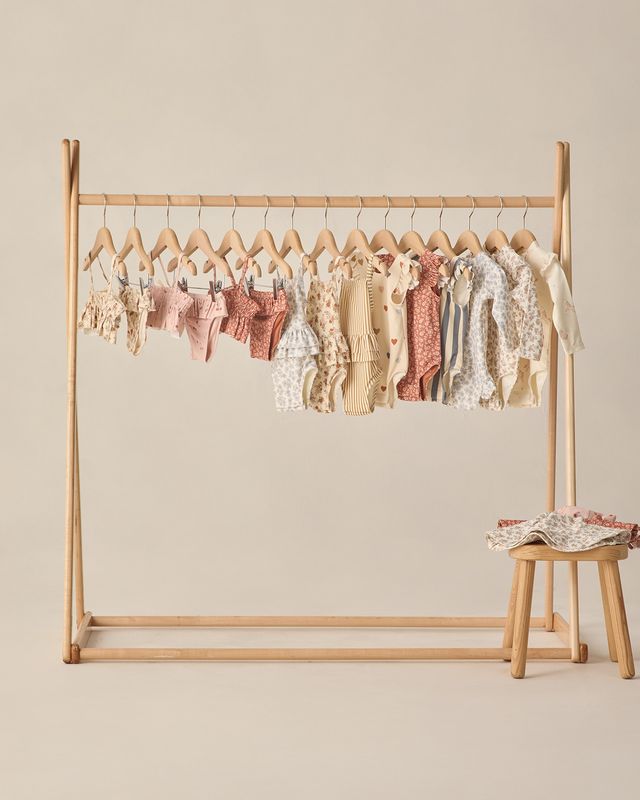 Wooden clothing rack with baby clothes on a beige background