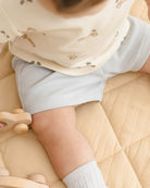 Close-up of a baby wearing a light-colored bib and shorts, sitting on a beige surface.