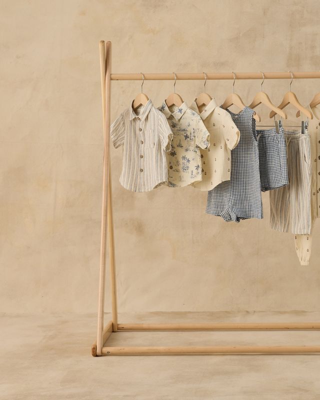 Wooden clothing rack with baby clothes on a beige background