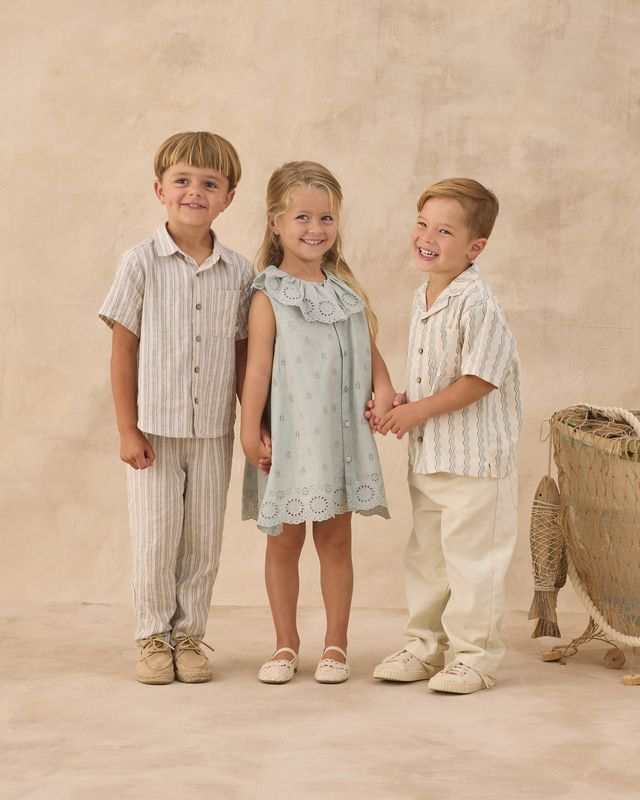 Three children standing together in a studio setting with a beige background