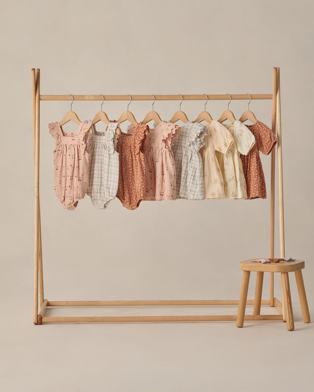 Wooden clothing rack with baby rompers on a beige background