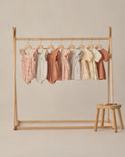 Wooden clothing rack with baby rompers on a beige background