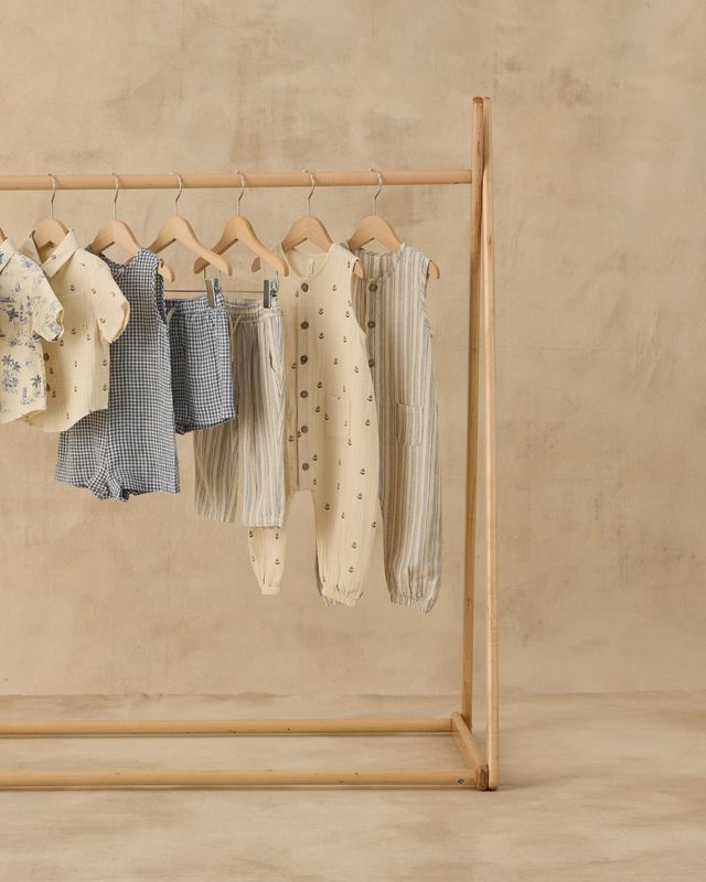 Wooden clothing rack with baby clothes on a beige background