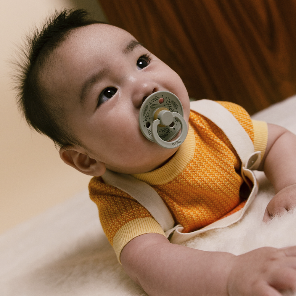 A child using a pacifiers with leaf patterns on a white and brown background
