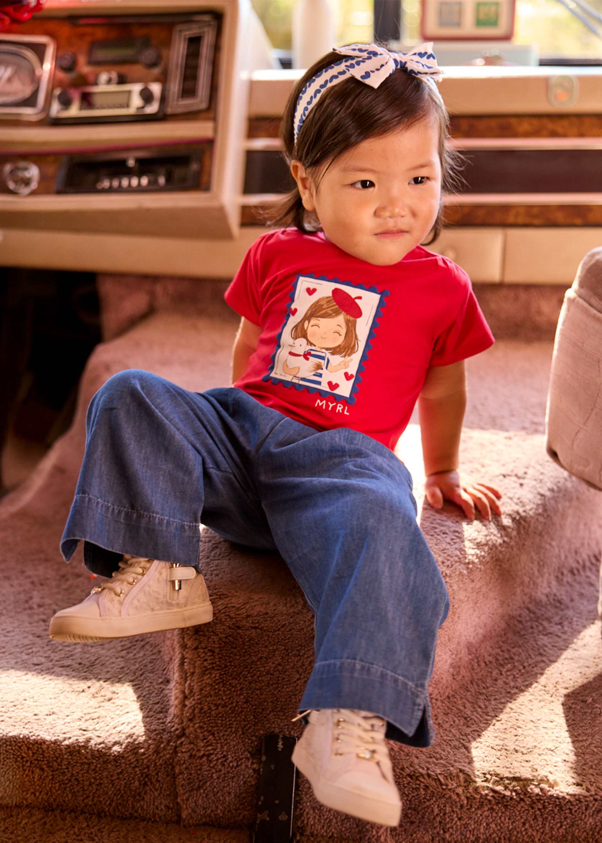 Child wearing a red shirt with a graphic design, sitting on a carpeted floor.