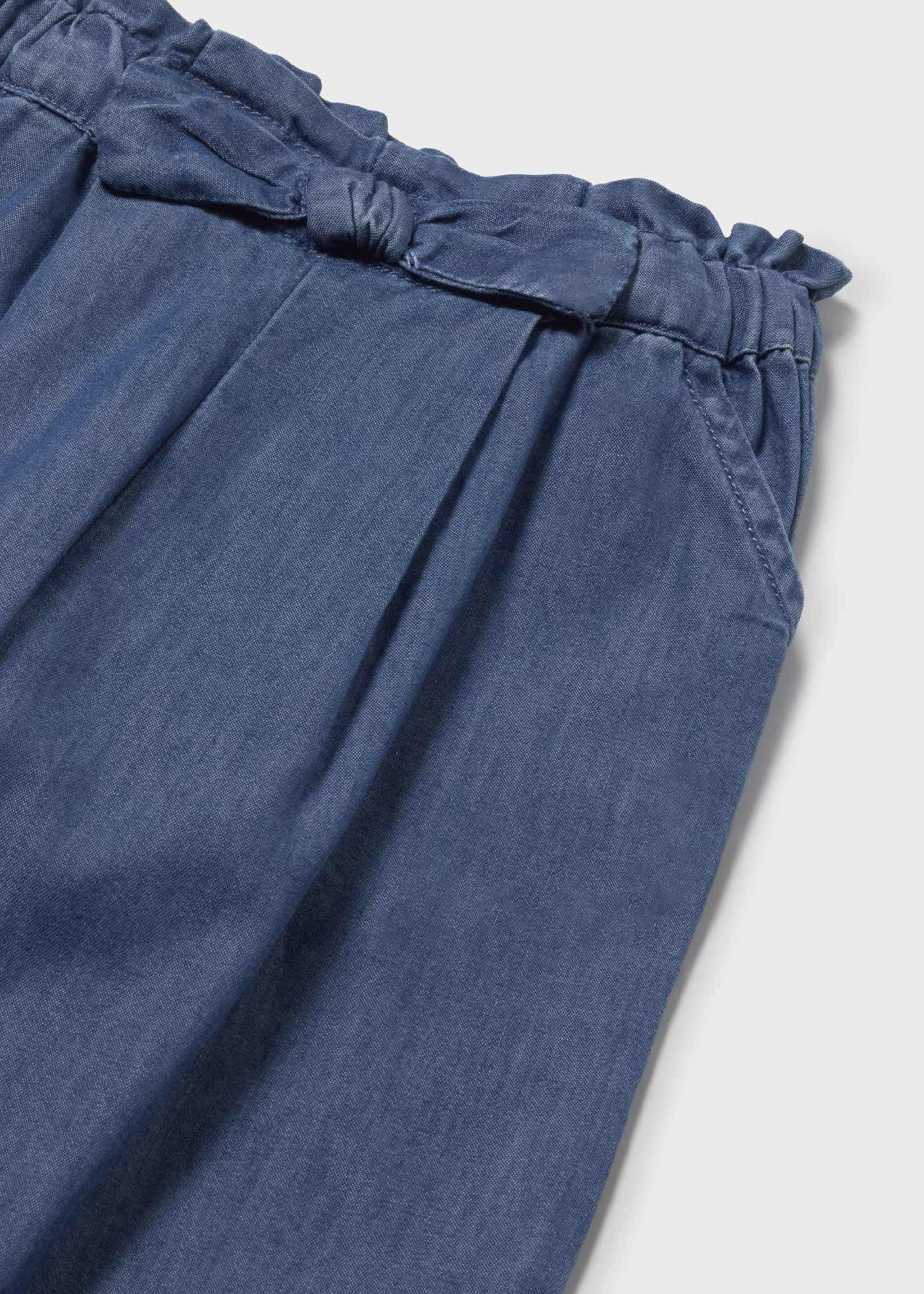 Blue denim pants with ruffled waistband on a light gray background