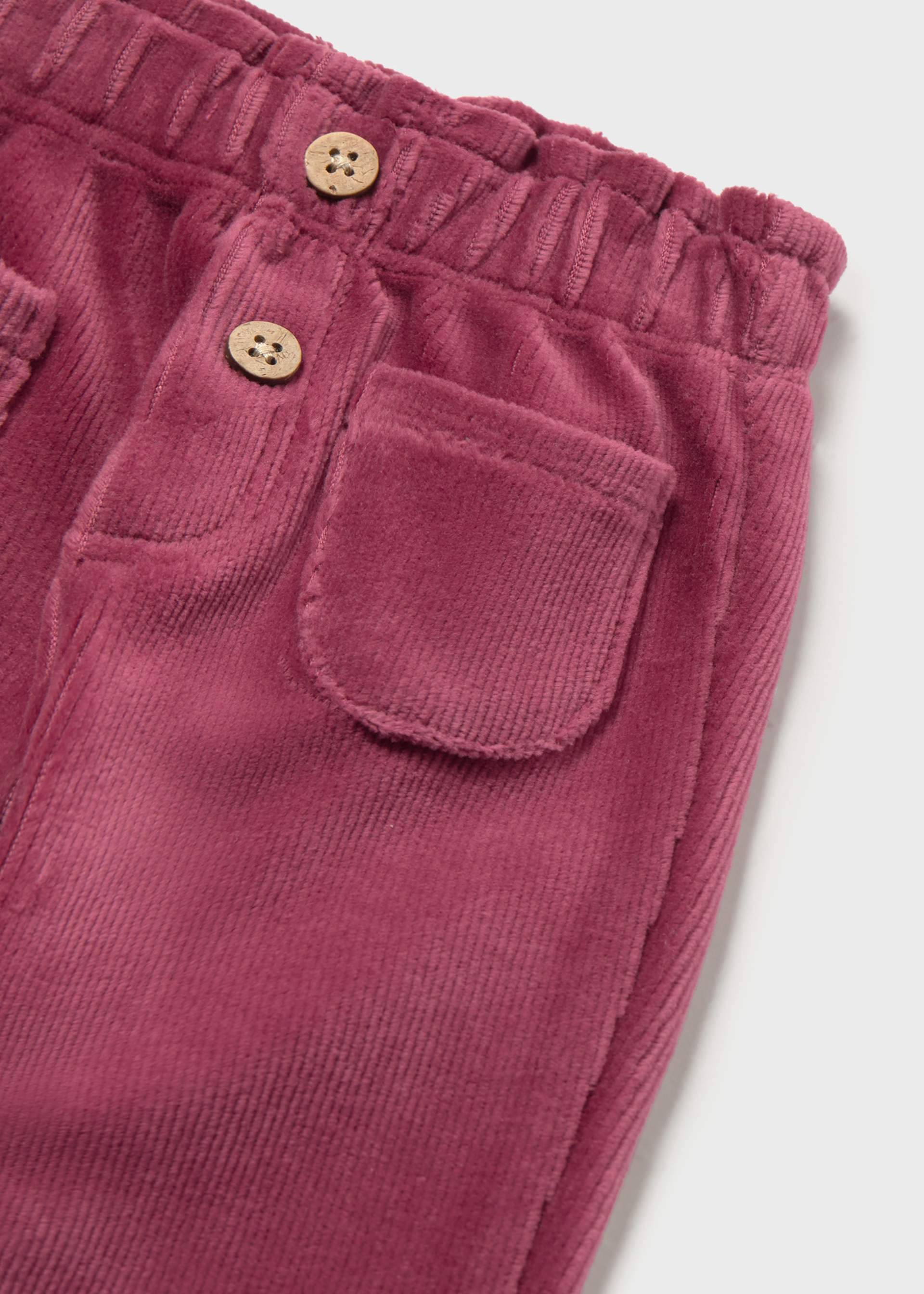 Close-up of dusty rose corduroy pants showing the elastic waistband, two decorative wooden buttons, and a front patch pocket.