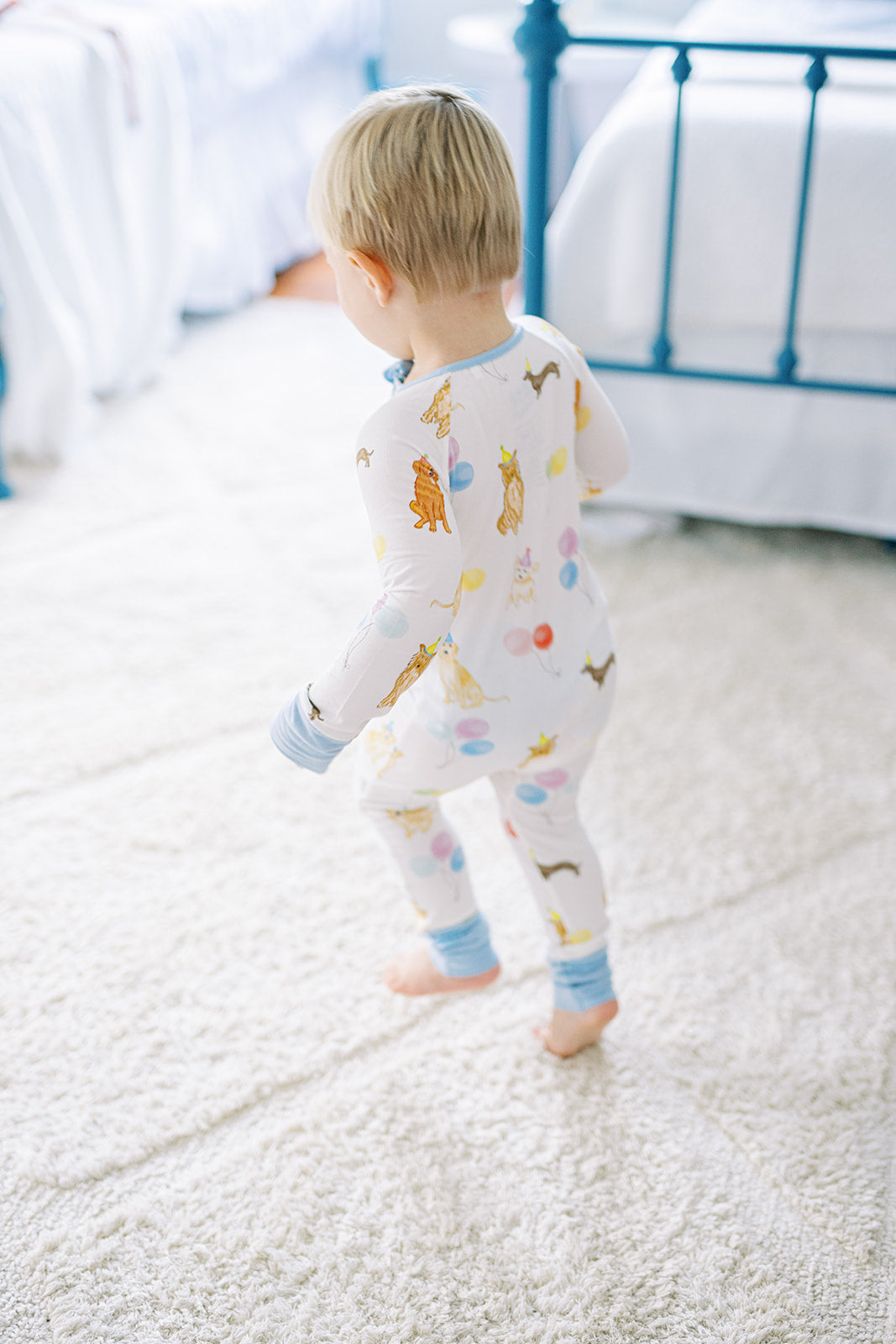 Child wearing a colorful onesie with animal prints on a carpeted floor.
