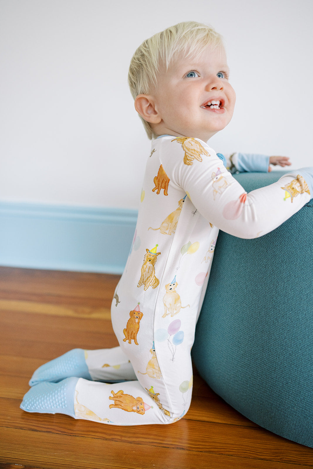 Child wearing a long-sleeve shirt with animal prints sitting on a wooden floor.