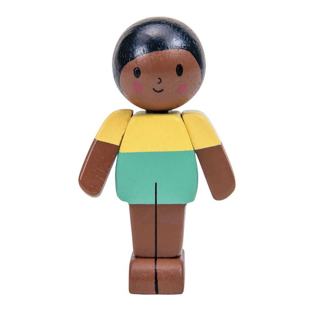 A wooden toy figure of a child with dark brown skin, black hair, a yellow top, and a mint green skirt, isolated on a white background.