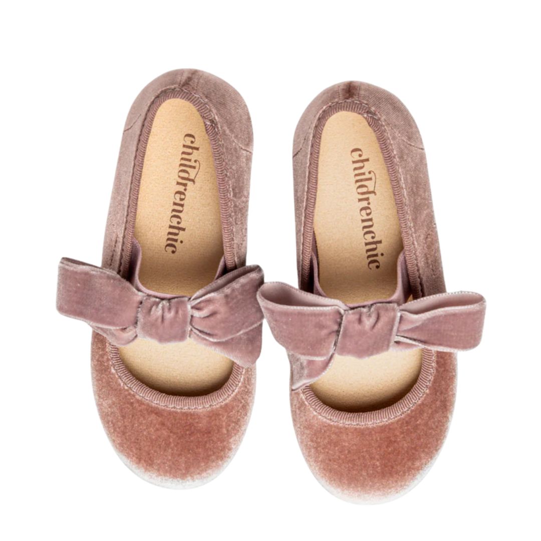 Pair of pink velvet shoes with bows on a white background