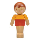 A wooden toy figure with a round head, brown hair, a yellow-orange shirt, and red shorts, shown on a plain white background.