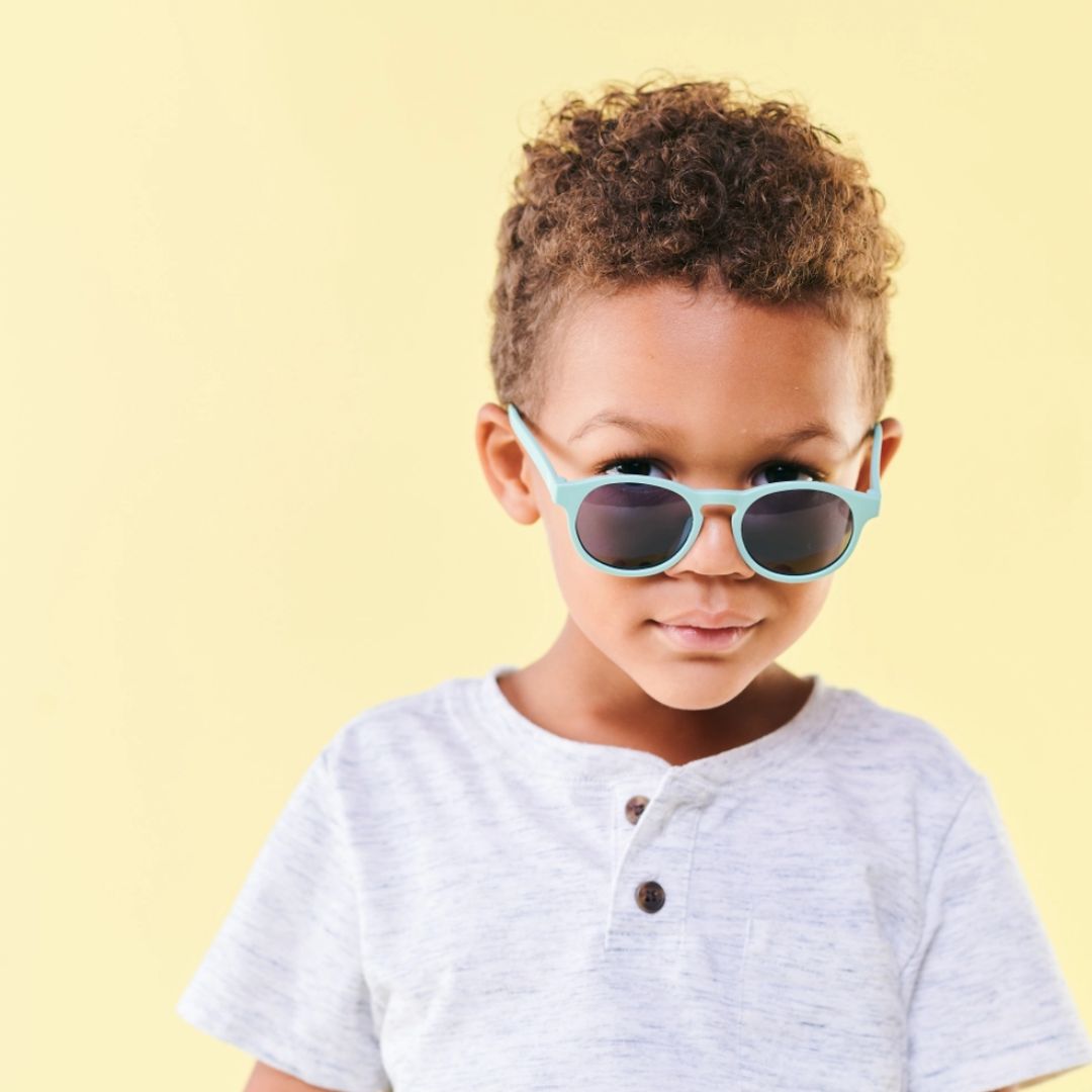 Child wearing light blue sunglasses against a yellow background