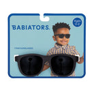 Babiators brand kids sunglasses in a black frame with dark lenses, shown on a blue retail card featuring the Babiators logo, age text 'Ages 0-2', and a child wearing the sunglasses.