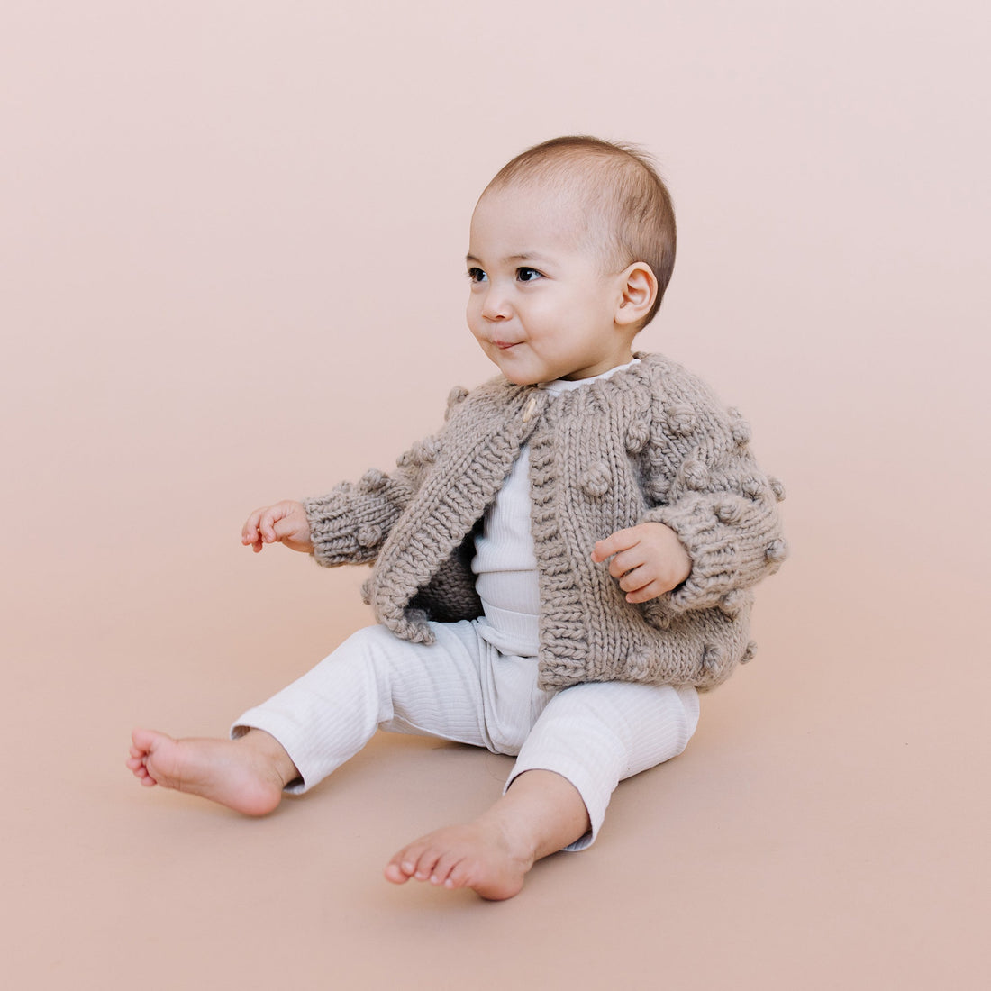 Baby wearing a knitted cardigan sitting on a beige background