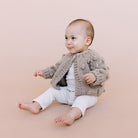 Baby wearing a knitted cardigan sitting on a beige background