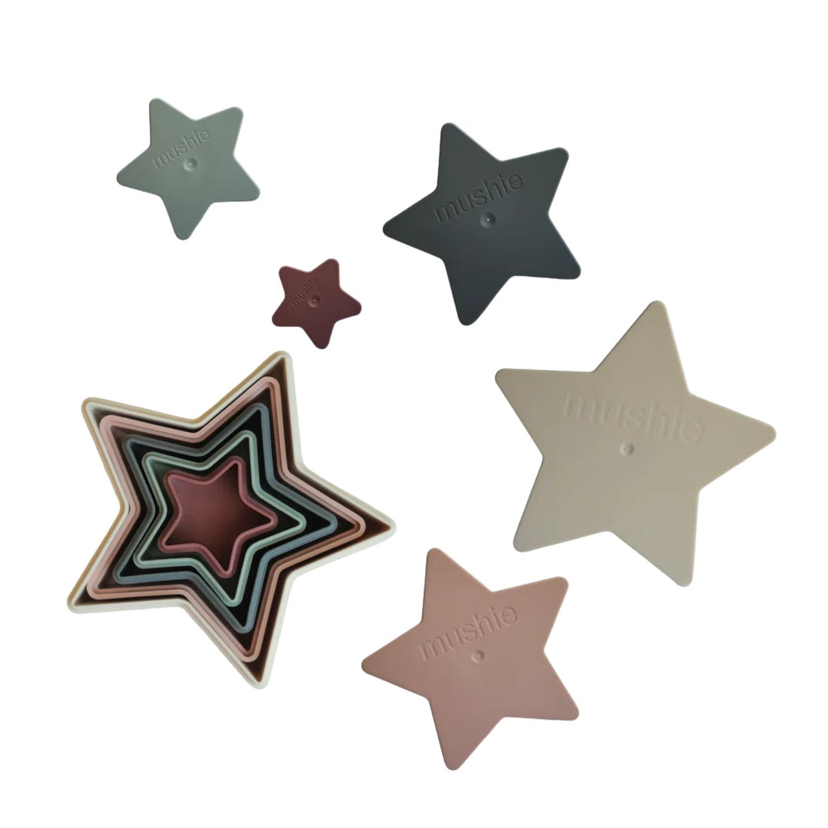 Six star-shaped silicone baby teething toys in various colors, including sage green, charcoal gray, mauve, beige, and dusty pink, arranged on a solid white background. The brand name 'mushio' is embossed on each star.