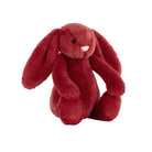 A plush red bunny toy with long floppy ears, black bead eyes, and a small white stitched nose, photographed on a plain white background.