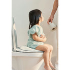 Child sitting on a toilet with a seat cover, holding toilet paper.