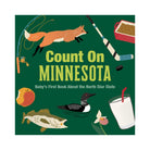 Front cover of the children's book 'Count On Minnesota' featuring a dark green background with illustrated Minnesota-themed elements including a fox fishing, hockey stick, lacrosse, loon, fish, apple, daffodil, and a milk glass. The title is printed in large yellow letters, with the subtitle 'Baby's First Book About the North Star State' below.