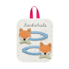 A children's hair accessory set on a white display card with a pink hanging loop. The set includes two light blue braided hair loops, each decorated with an orange fox head and a pale green bow tie, plus the word 'Rockahula' printed on the card.