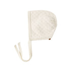 An off-white knit bonnet with a textured diamond pattern and a matching braided chin strap, shown on a plain white background.