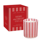 A 12 oz scented candle by Sweet Water Decor with its red packaging box. The candle features red and white vertical stripes on a clear glass vessel, and the box is red with white text reading 'MERRY and BRIGHT'.