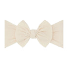 A cream-colored fabric bow headband with a knotted center and small embroidered dots, shown against a plain white background.
