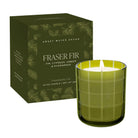 A 12 oz scented candle by Sweet Water Decor in a translucent olive green glass jar with a white wick and flame, shown next to its matching dark green box with botanical illustrations and the scent name Fraser Fir.